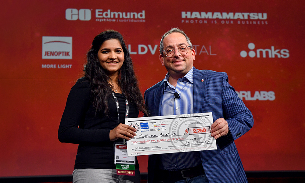 A female winner from SPIE Startup Challenge accept a large check from Jason Eichenhauer
