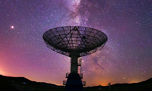A sky of pink, blue, and purple surround stars to make up the backdrop of a radio telescope