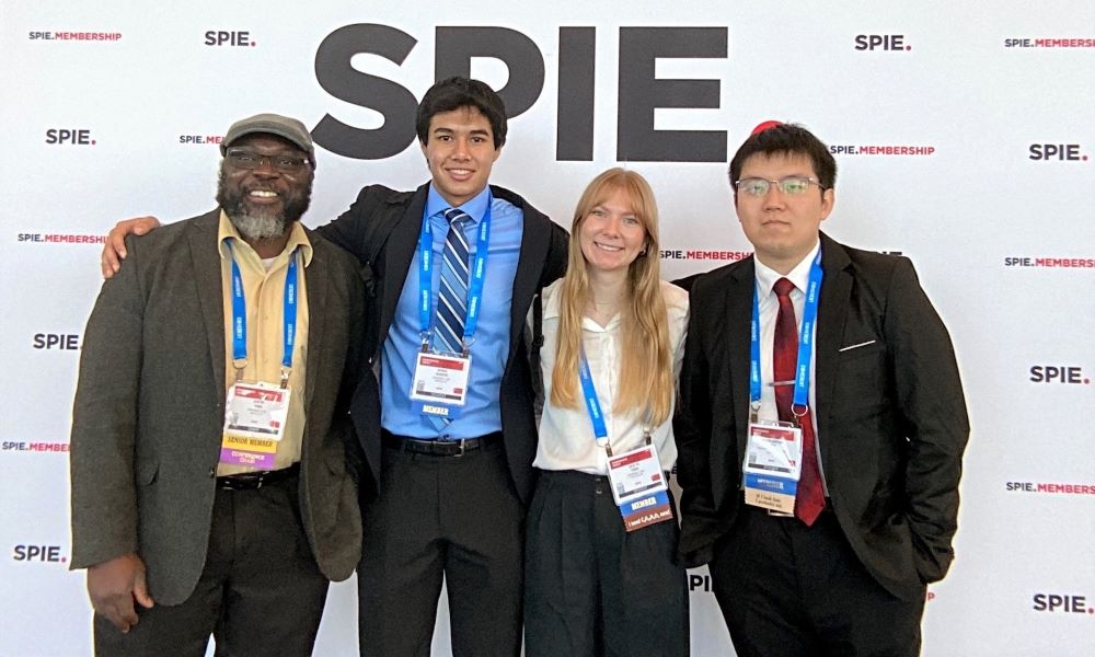A group of three students and a chapter advisor standing together in front of the SPIE Membership photo booth backdrop
