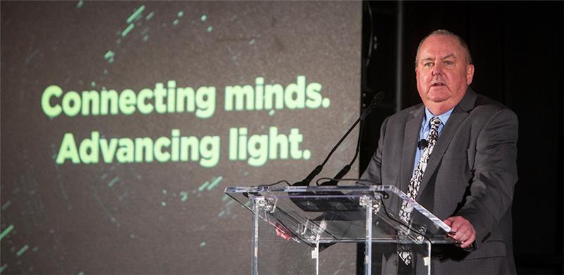 2020 SPIE President John Greivenkamp at the Sunday evening plenary at 2021 SPIE Optics + Photonics conference with SPIE tagline "Connecting minds. Advancing light" in the background.